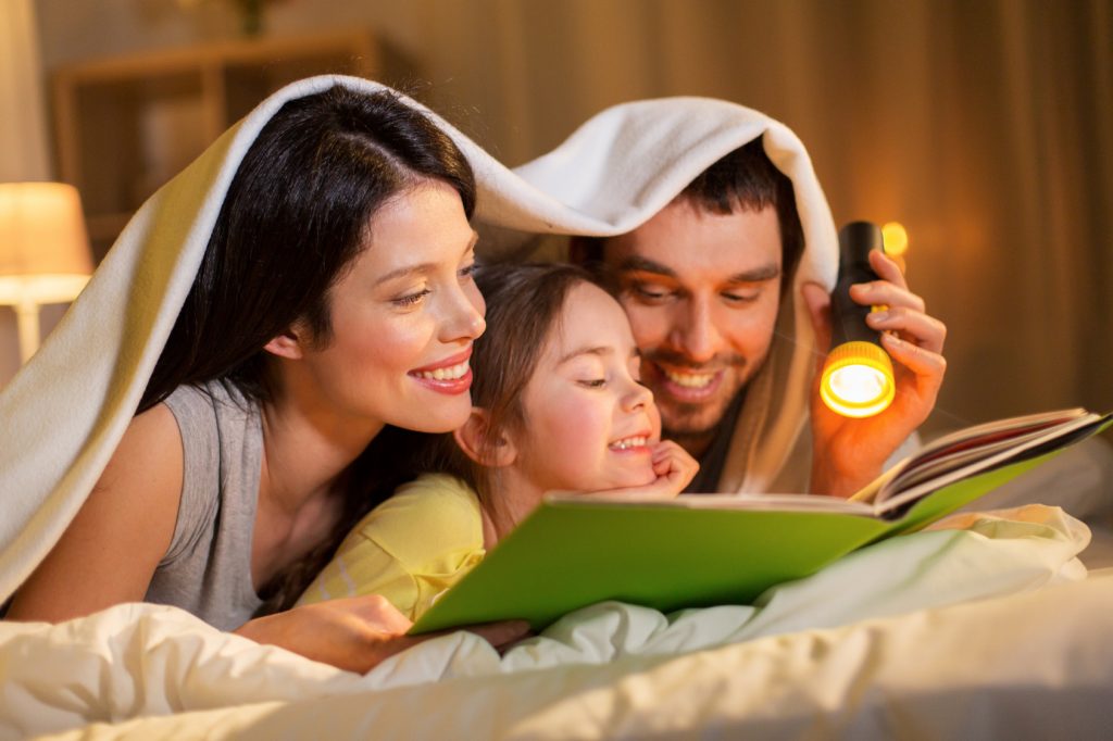 Aile içi iletişimde kilit noktalar: yatakta çocuklarıyla kştap okuyan mutlu anne ve baba