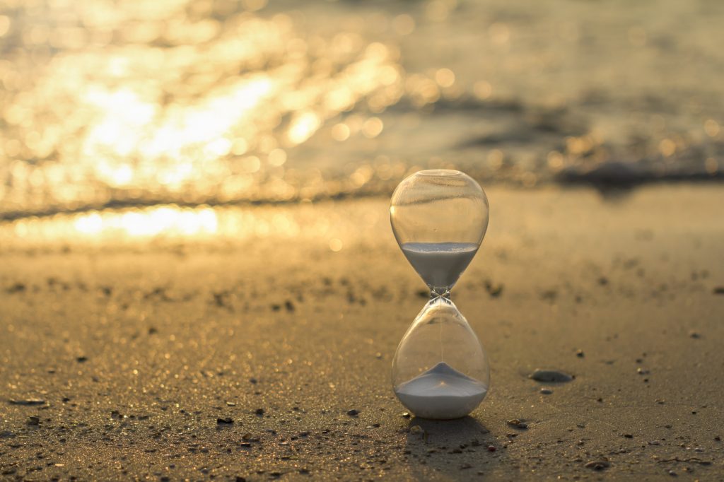 Hayatı ve zamanı tüketiyoruz. Sahilde akan bir kum saati fotoğrafı.